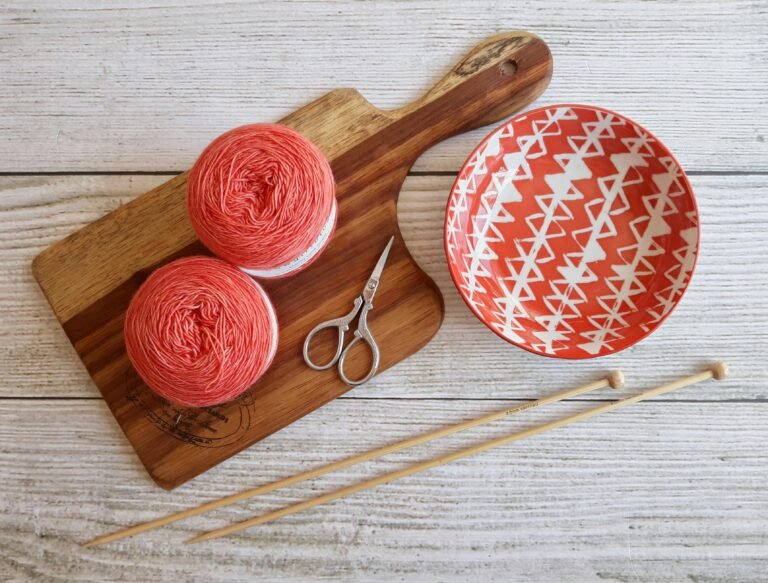 Home Aesthetic flat lay of yarn balls, knitting needles, and patterned bowl on a wooden board.